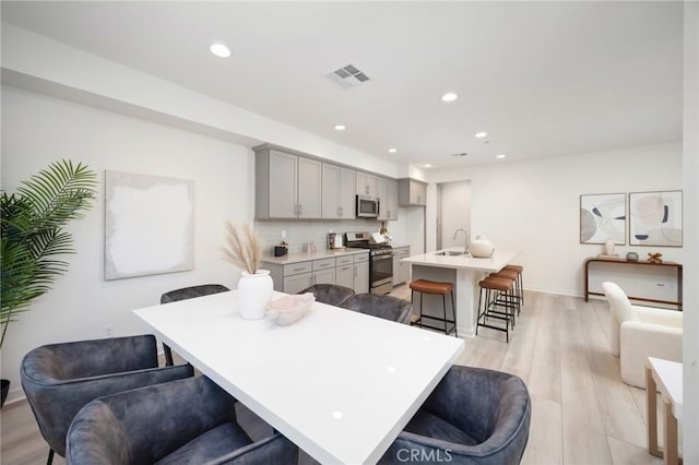 kitchen with appliances with stainless steel finishes, gray cabinetry, a kitchen island with sink, a kitchen breakfast bar, and sink