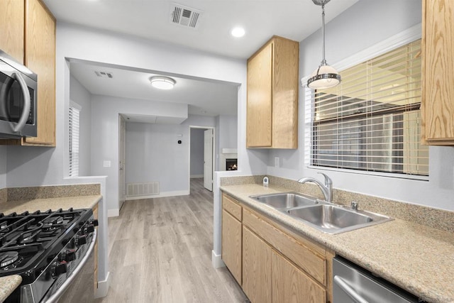 kitchen with appliances with stainless steel finishes, light brown cabinetry, sink, pendant lighting, and light hardwood / wood-style floors