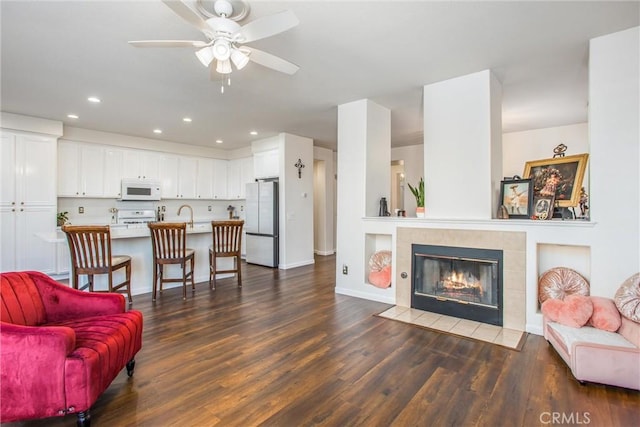 living room featuring a tile fireplace, dark hardwood / wood-style flooring, and ceiling fan