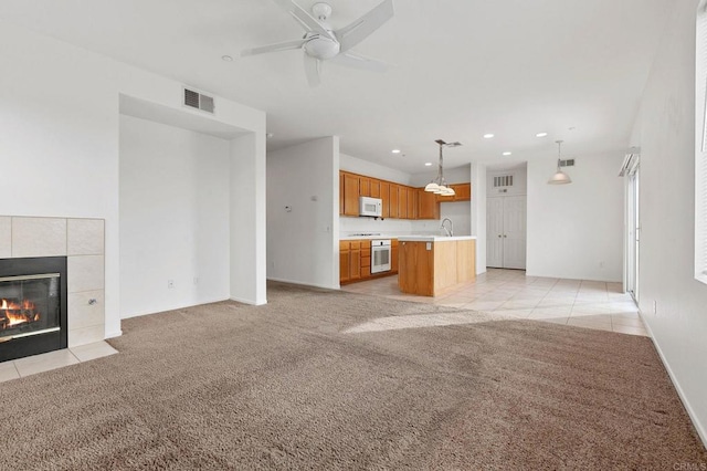 unfurnished living room with ceiling fan, sink, a tile fireplace, and light carpet