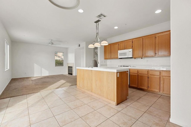 kitchen featuring ceiling fan, hanging light fixtures, sink, light tile patterned floors, and an island with sink