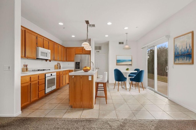 kitchen with white appliances, a center island with sink, hanging light fixtures, and light tile patterned flooring