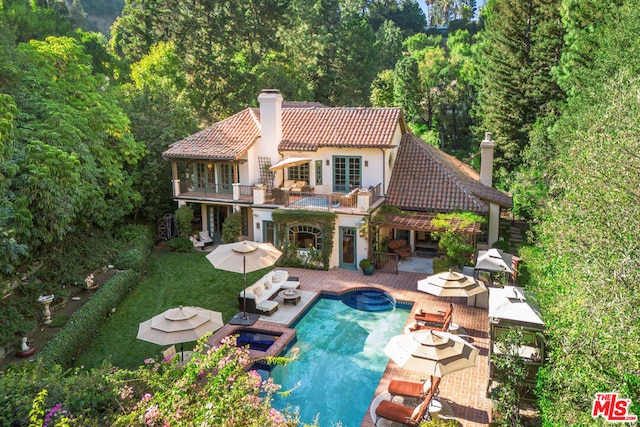 rear view of house featuring outdoor lounge area, a swimming pool with hot tub, a balcony, and a patio area