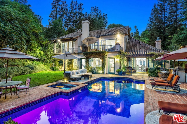 rear view of property featuring a lawn, a pool with hot tub, an outdoor hangout area, a balcony, and a patio area