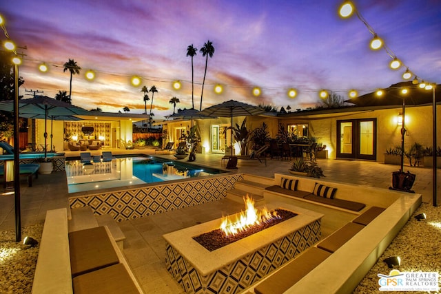 pool at dusk featuring french doors, an outdoor living space with a fire pit, and a patio area