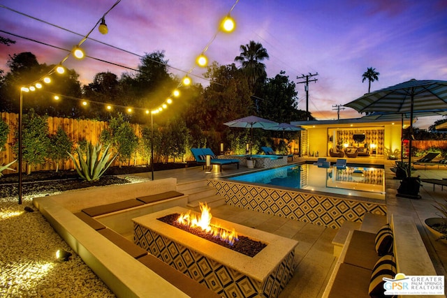 pool at dusk with a patio and an outdoor fire pit