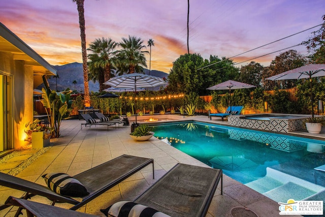 pool at dusk featuring a mountain view, a patio area, and an in ground hot tub