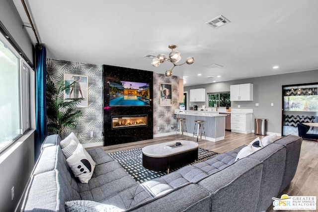 living room featuring a high end fireplace, light wood-type flooring, plenty of natural light, and a notable chandelier