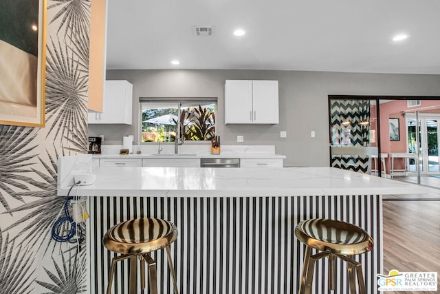 kitchen featuring white cabinets, a kitchen breakfast bar, sink, light stone countertops, and light wood-type flooring