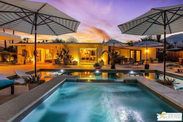 pool at dusk featuring an in ground hot tub and a patio