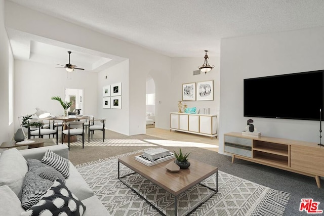 carpeted living room with a textured ceiling, high vaulted ceiling, and ceiling fan