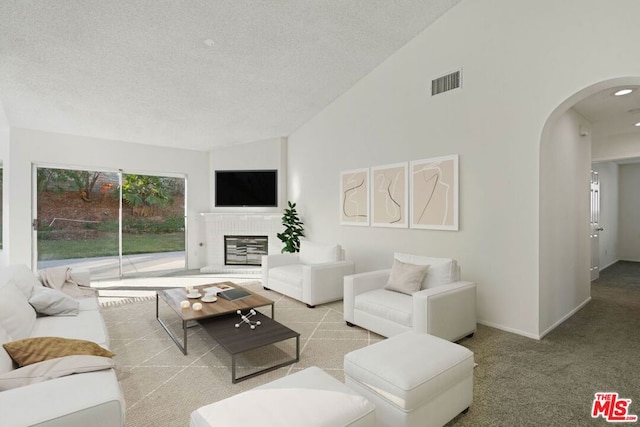 carpeted living room with a textured ceiling, high vaulted ceiling, and a brick fireplace