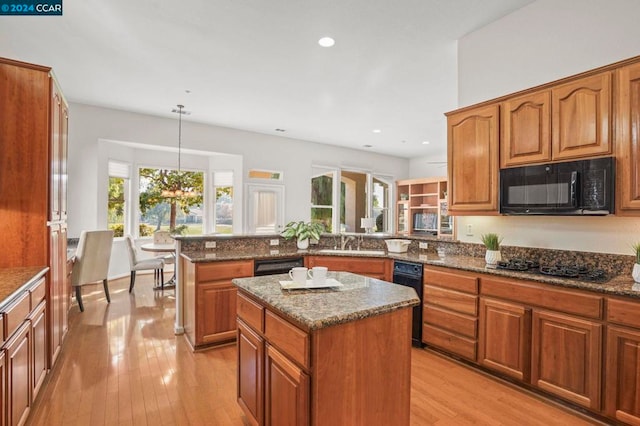 kitchen with black appliances, decorative light fixtures, dark stone countertops, a center island, and light hardwood / wood-style floors