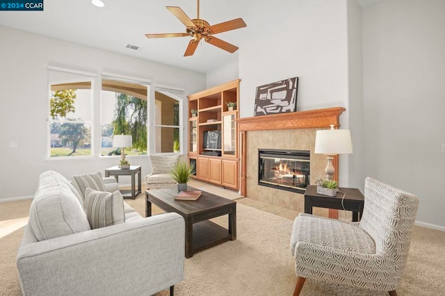 living room featuring a tiled fireplace, light carpet, and ceiling fan