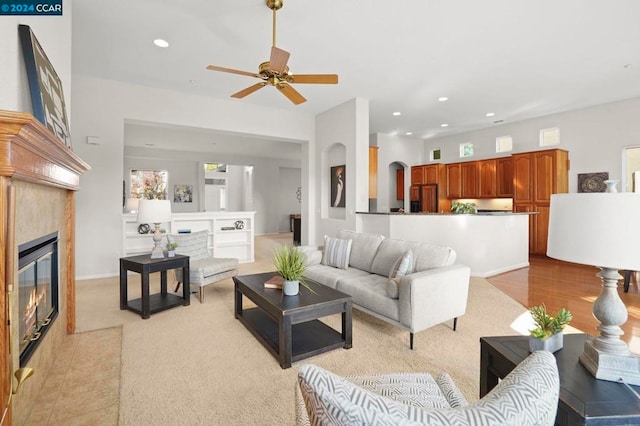 living room featuring ceiling fan, light carpet, and a tile fireplace