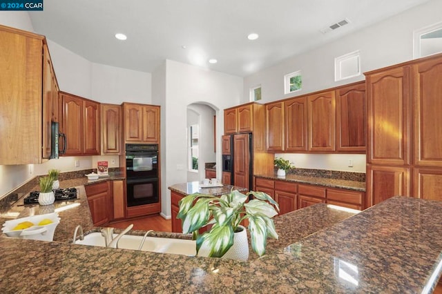 kitchen featuring sink, a kitchen breakfast bar, dark stone countertops, black appliances, and hardwood / wood-style flooring