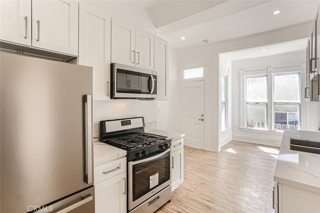 kitchen featuring light wood-type flooring, stainless steel appliances, white cabinetry, and light stone counters