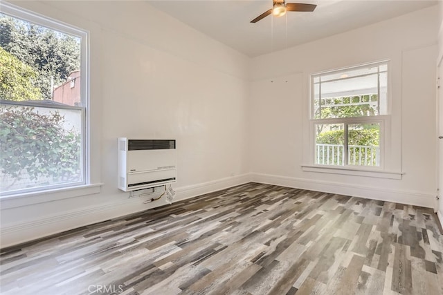 unfurnished room with hardwood / wood-style floors, heating unit, ceiling fan, and a healthy amount of sunlight