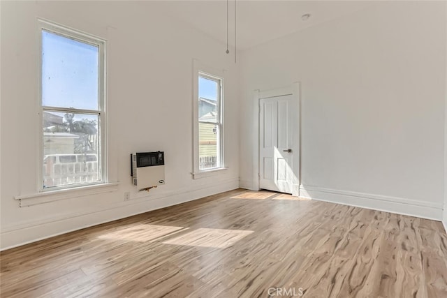 spare room featuring a healthy amount of sunlight, light hardwood / wood-style flooring, and heating unit