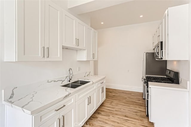 kitchen featuring stove, white cabinets, sink, light stone countertops, and light hardwood / wood-style floors