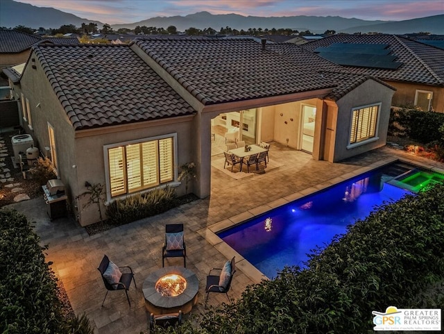 back house at dusk with a fire pit, a mountain view, and a patio area