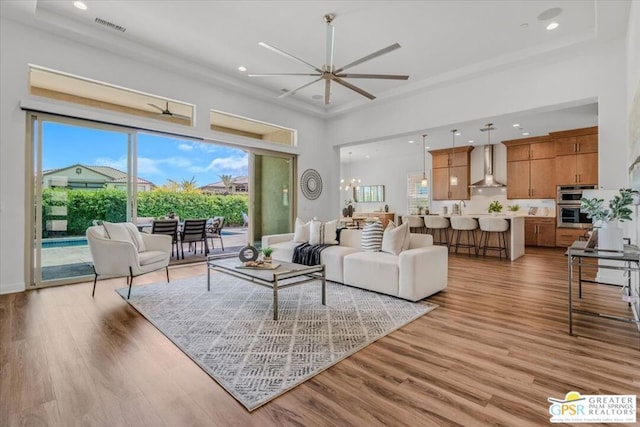 living room with ceiling fan with notable chandelier, light hardwood / wood-style floors, and a wealth of natural light