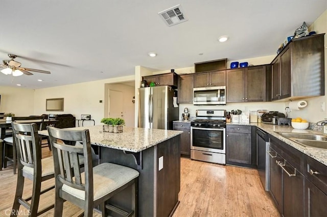 kitchen featuring light stone countertops, appliances with stainless steel finishes, light wood-type flooring, a breakfast bar, and sink