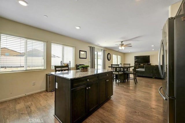 kitchen with hardwood / wood-style floors, a center island, ceiling fan, stainless steel fridge, and light stone countertops