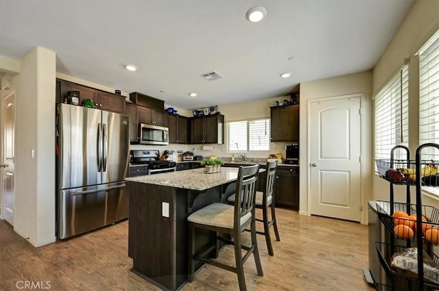 kitchen featuring appliances with stainless steel finishes, light wood-type flooring, a breakfast bar, dark brown cabinetry, and a center island