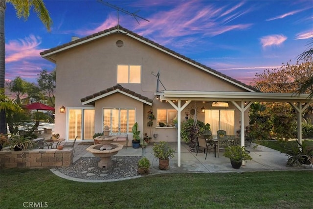 back house at dusk with a patio and a lawn