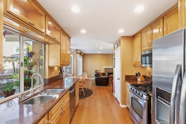 kitchen featuring sink, stainless steel appliances, light hardwood / wood-style flooring, dark stone counters, and a fireplace