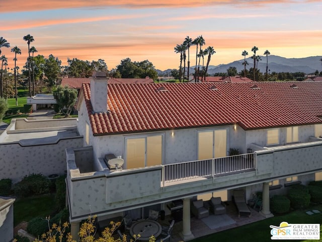 back house at dusk with a mountain view, a balcony, and a patio