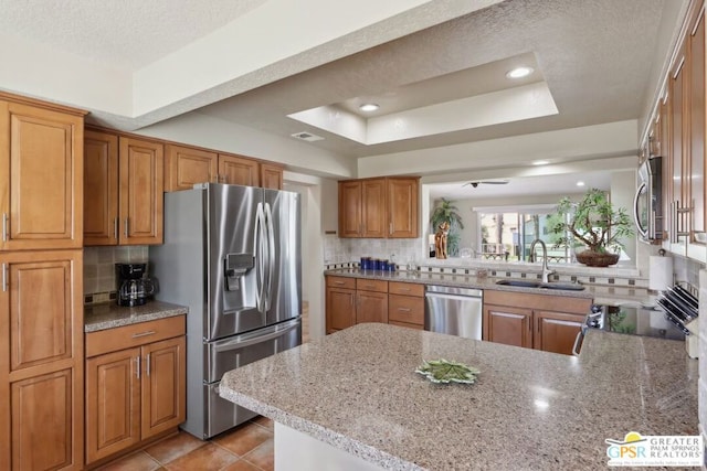 kitchen with sink, stainless steel appliances, kitchen peninsula, a tray ceiling, and decorative backsplash