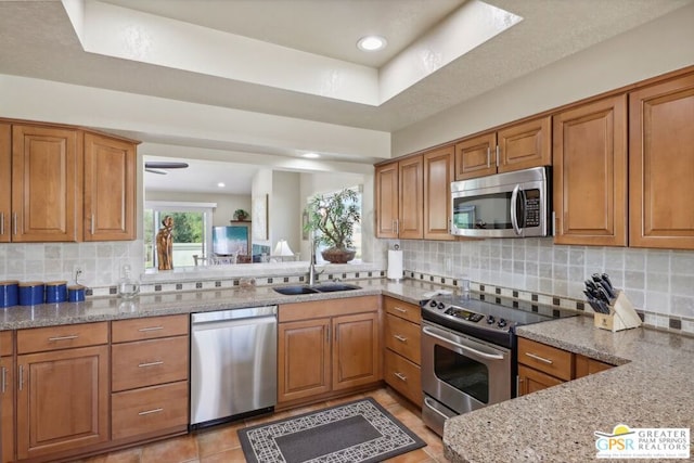 kitchen with tasteful backsplash, light stone counters, stainless steel appliances, sink, and light tile patterned floors