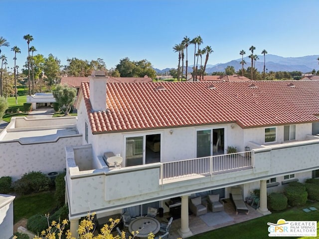 rear view of property featuring a mountain view, a balcony, and a patio