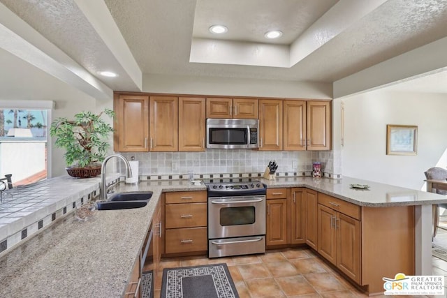 kitchen with kitchen peninsula, appliances with stainless steel finishes, tasteful backsplash, a raised ceiling, and sink