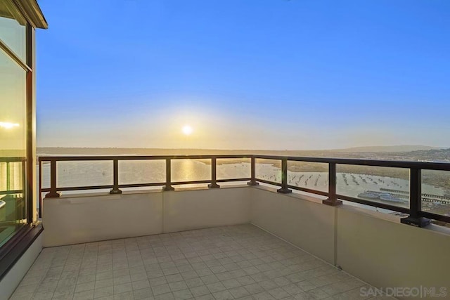 balcony at dusk featuring a water view