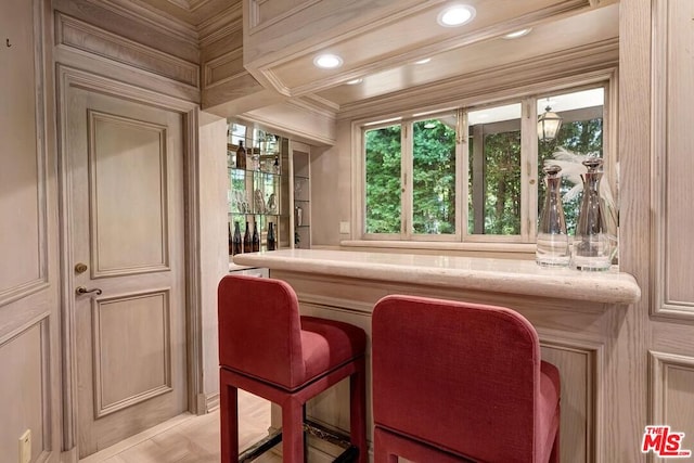 bar with light stone counters, ornamental molding, and cream cabinets