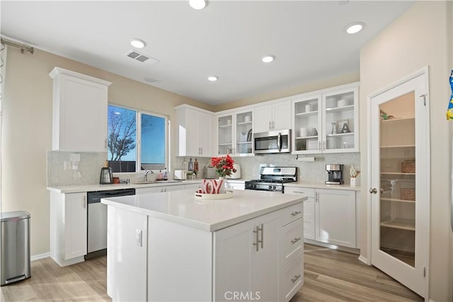 kitchen with appliances with stainless steel finishes, light wood-type flooring, white cabinetry, and a kitchen island