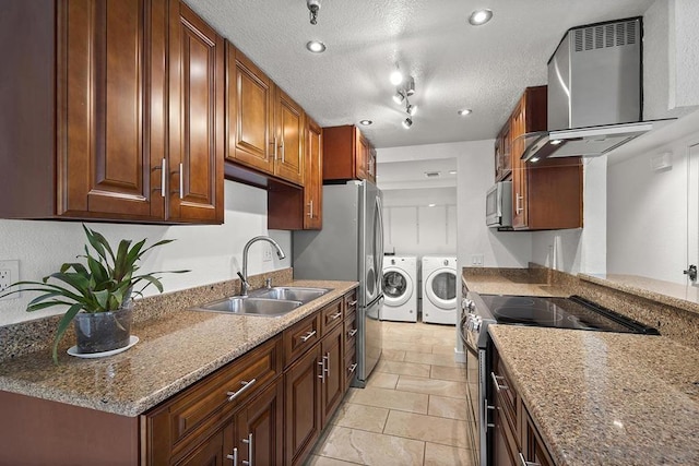 kitchen featuring sink, light stone counters, stainless steel appliances, washing machine and dryer, and wall chimney exhaust hood