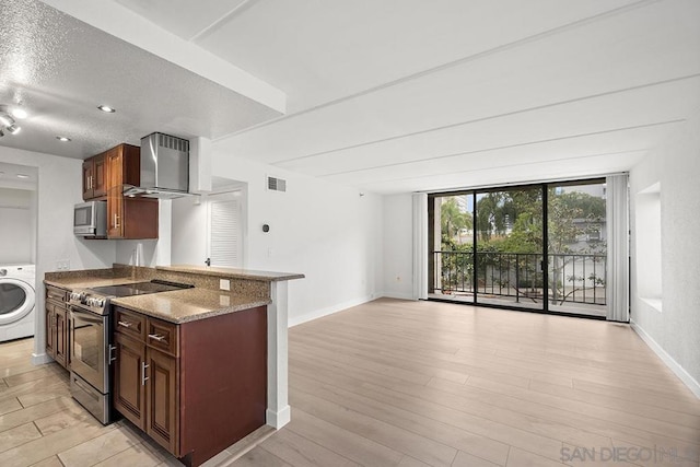 kitchen featuring wall chimney range hood, appliances with stainless steel finishes, light stone countertops, washer / dryer, and kitchen peninsula