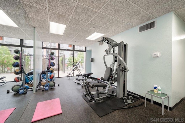 exercise room featuring a paneled ceiling and a wall of windows