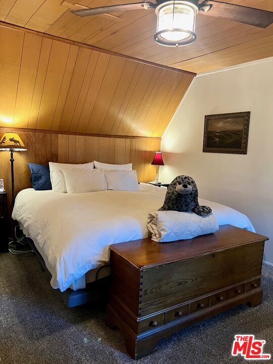 carpeted bedroom with vaulted ceiling, wooden ceiling, and wood walls