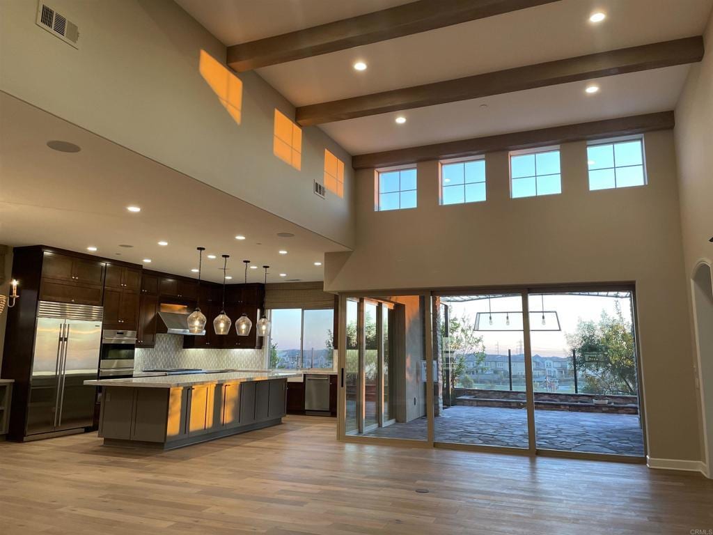 kitchen featuring appliances with stainless steel finishes, light countertops, light wood-style floors, beam ceiling, and exhaust hood