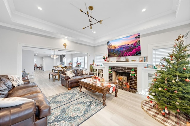 living room featuring a raised ceiling, crown molding, a fireplace, and light hardwood / wood-style floors