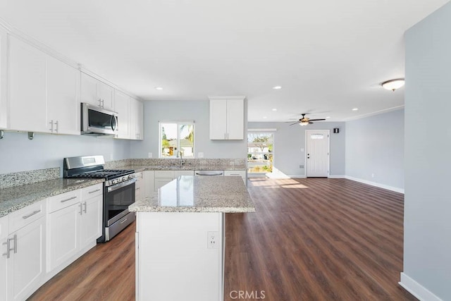 kitchen featuring ceiling fan, a center island, stainless steel appliances, white cabinets, and light stone counters