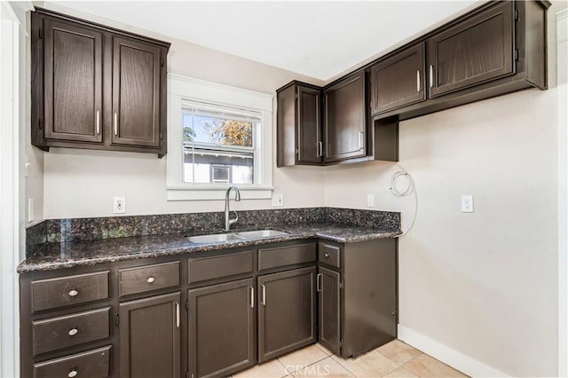 kitchen featuring light tile patterned flooring, sink, dark brown cabinetry, and dark stone counters