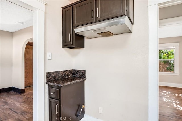 kitchen with dark brown cabinets, dark stone countertops, and hardwood / wood-style floors