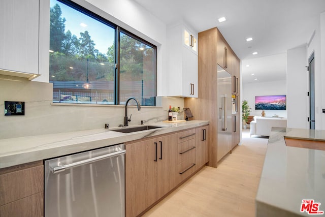 kitchen with light stone countertops, sink, light hardwood / wood-style flooring, stainless steel dishwasher, and white cabinets