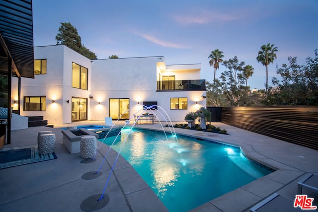 pool at dusk featuring pool water feature and an in ground hot tub